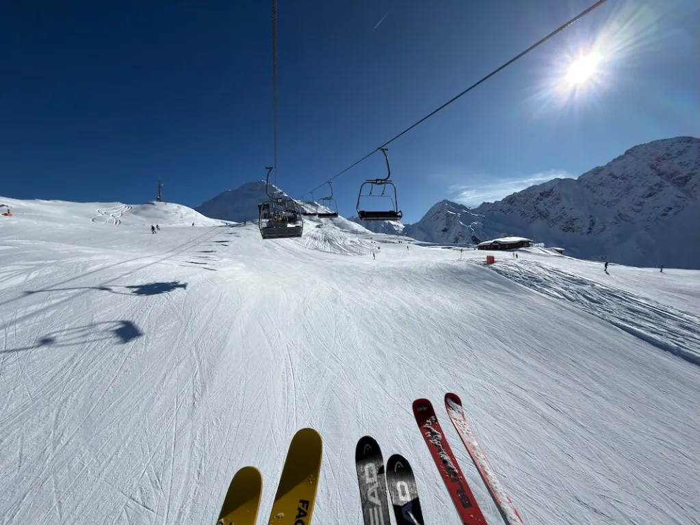 Chairlift ride in the Brunnalm ski area – skis in the foreground, mountain panorama and Weißspitzhütte in the background